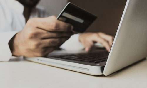 A close-up view of a man at a laptop holding a credit card