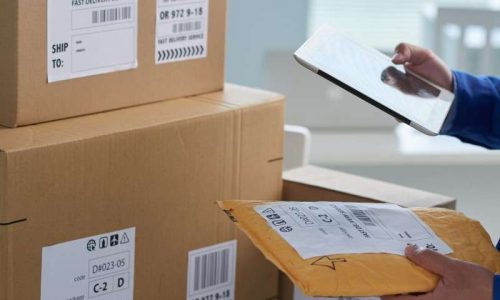 Freight delivery person checking labels on packaging with tablet